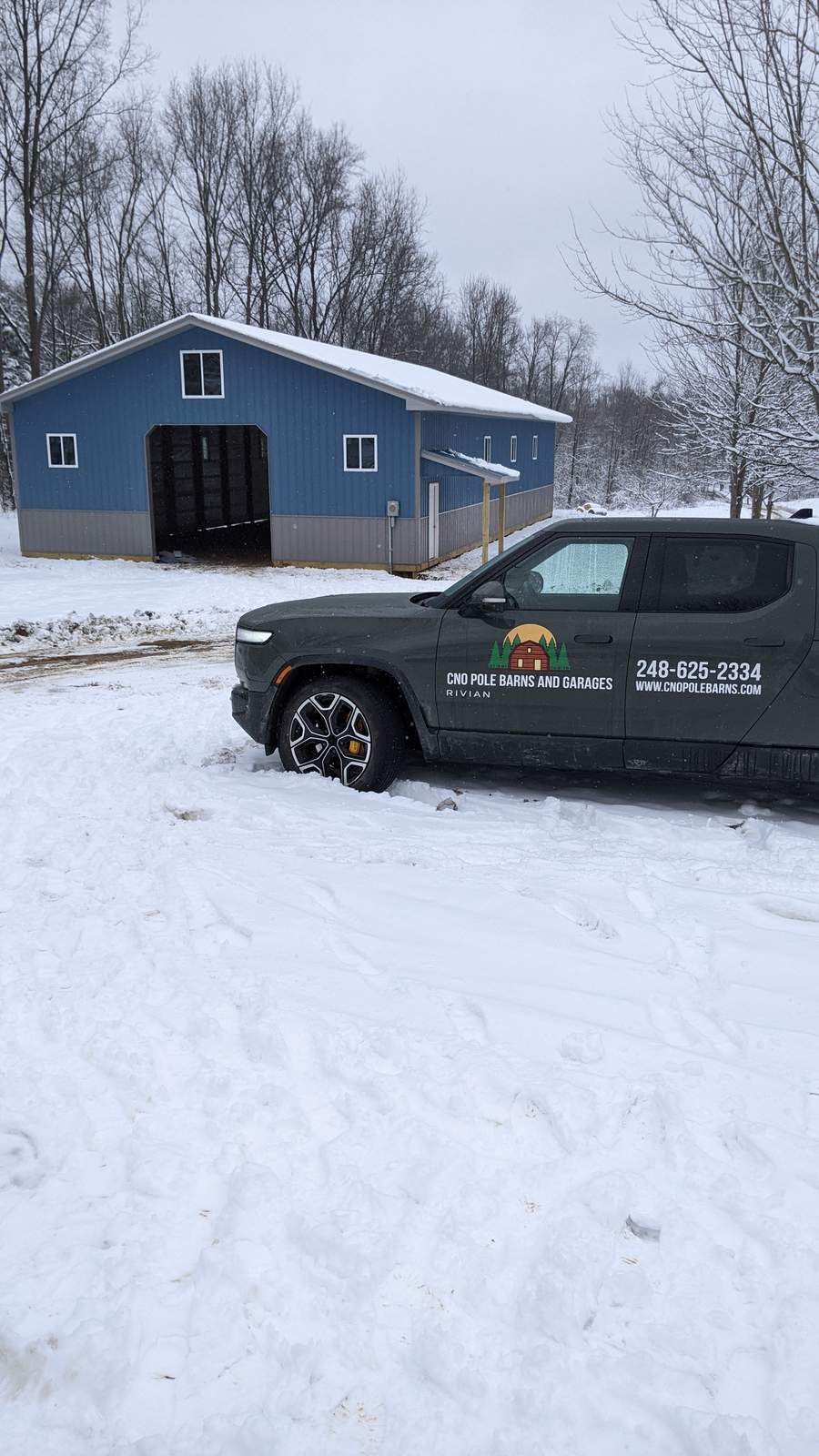 Blue and gray pole barn exterior in snow, portrait view showing full gable end