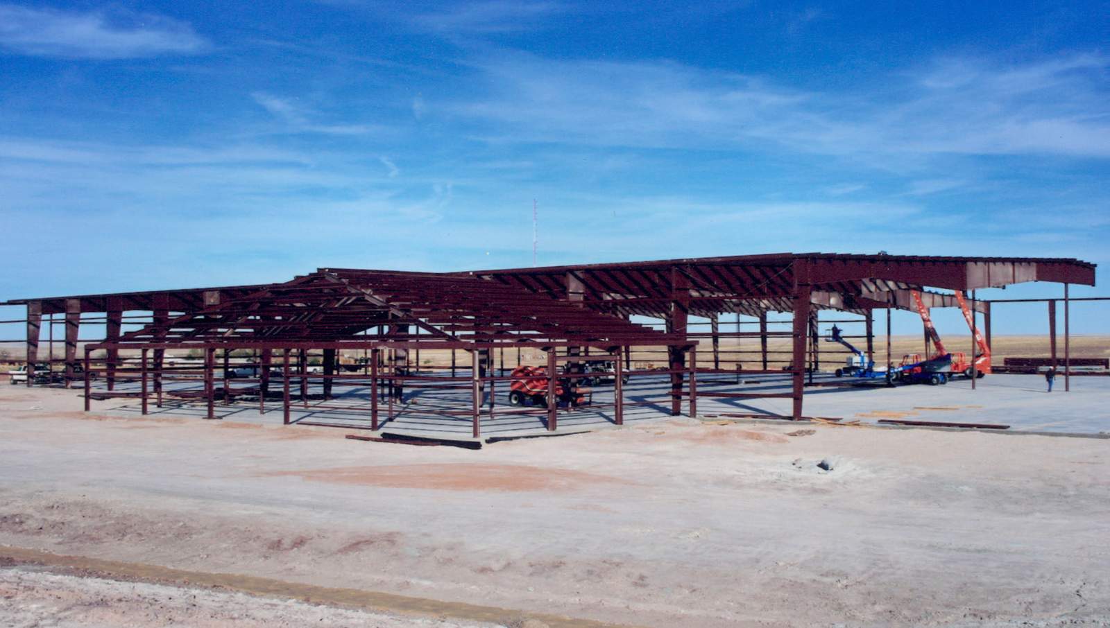 Long steel frame of an industrial building mid-construction, columns and rafters in place