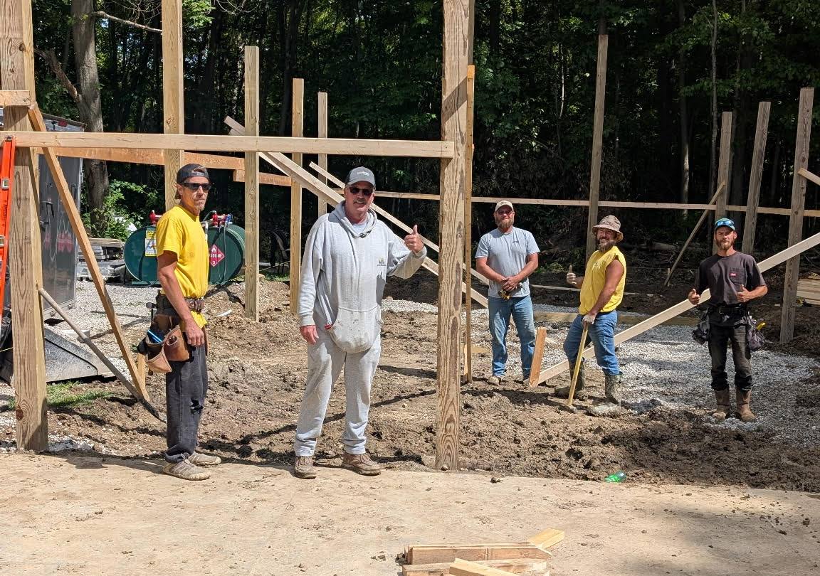 Five CNO crew members on a job site with barn posts set behind them